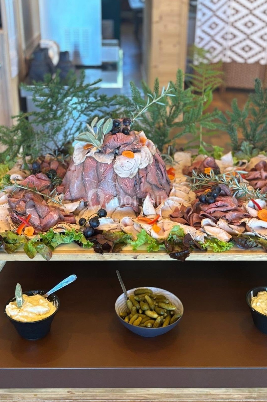 Plateau de charcuterie garnie de légumes, herbes fraîches et olives, accompagné de condiments et sauces en bols.