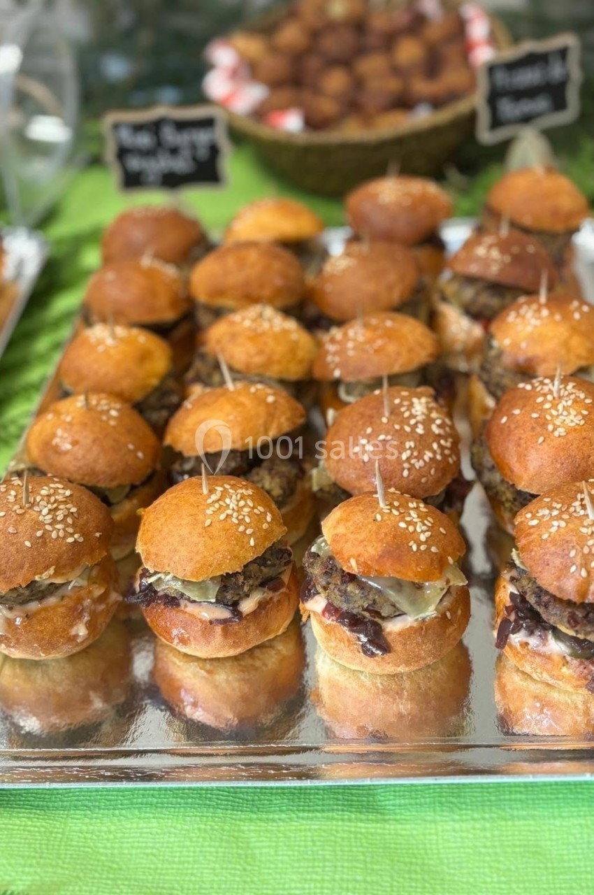 Plateau de mini-burgers garnis de fromage fondu et d'oignons caramélisés, présentés sur une nappe verte.