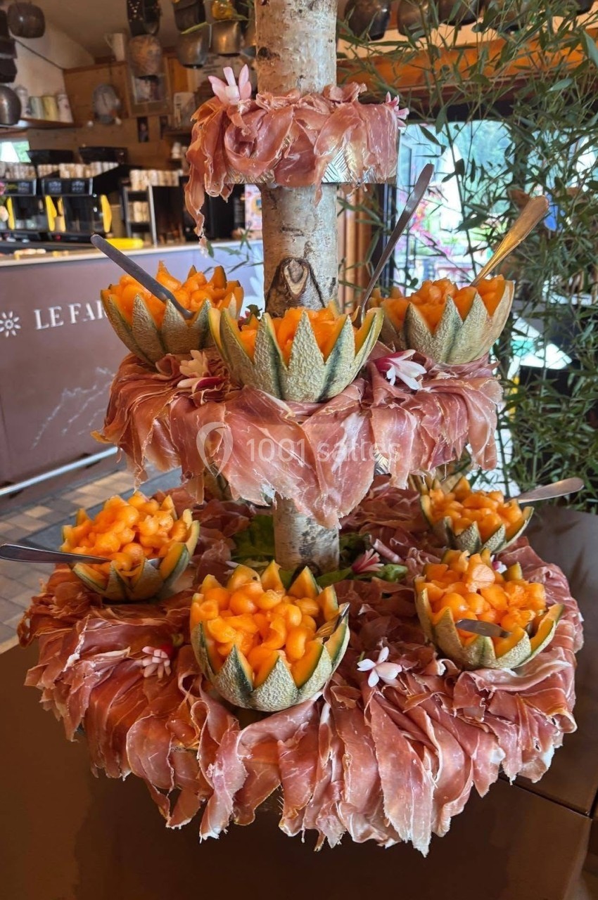 Présentoir en bois garni de tranches de jambon et de bols de melon coupé, décoré de fleurs.