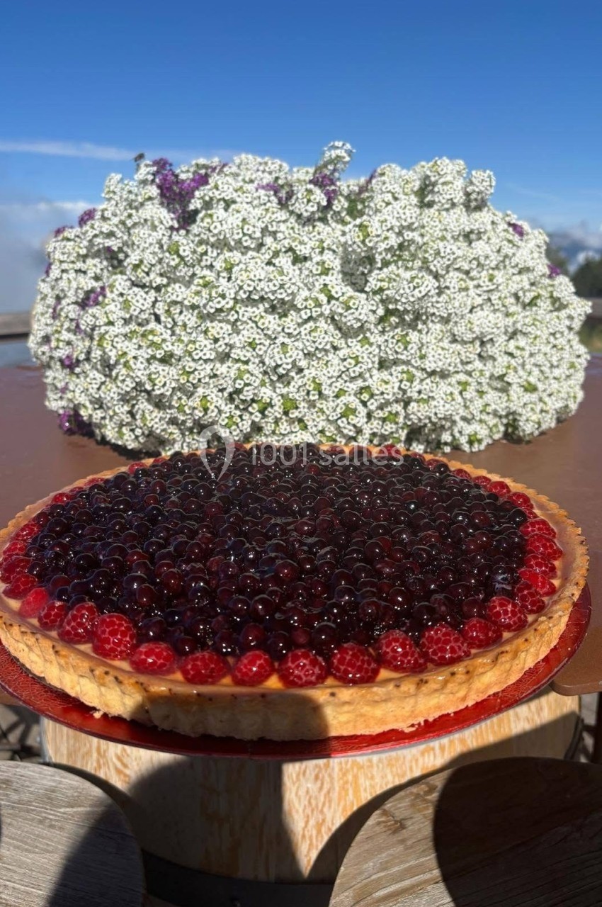 Tarte aux fruits rouges sur une table en bois, avec un bouquet de fleurs blanches en arrière-plan.
