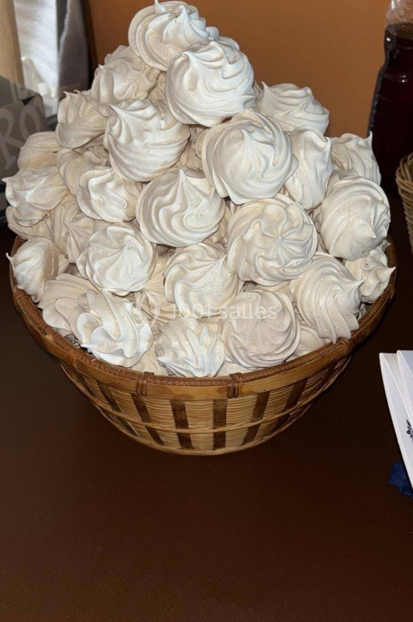 Panier en osier rempli de meringues blanches disposées en pyramide sur une table marron.