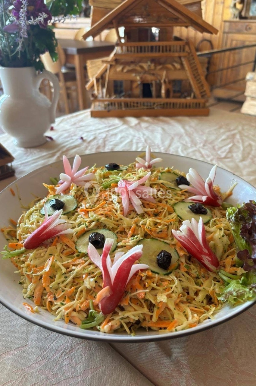 Salade colorée garnie de légumes râpés, radis sculptés, olives noires et feuilles de salade, sur une table rustique.