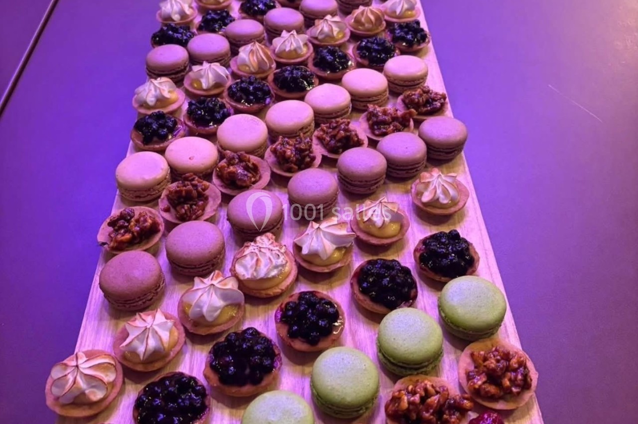 Plateau en bois garni de macarons colorés, tartelettes aux fruits et pâtisseries variées disposés en rangées.