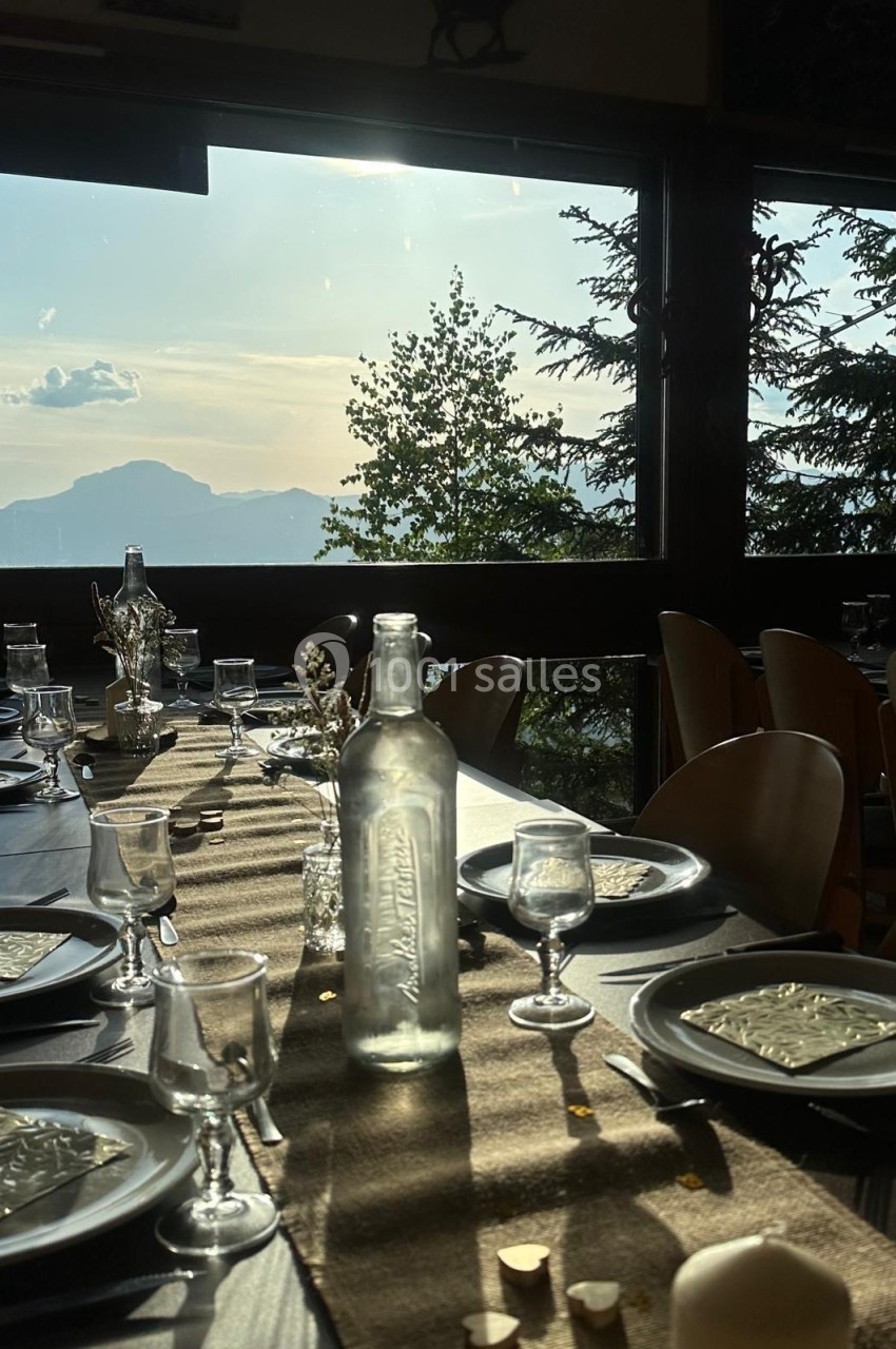 Table dressée avec vaisselle et carafe en verre, éclairée par la lumière du soleil couchant, avec vue sur des montagnes.