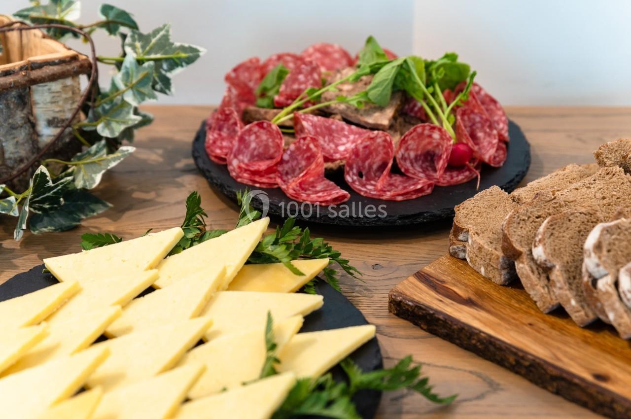 Plateaux de charcuterie, fromage et pain sur une table en bois, décorée de feuilles vertes.