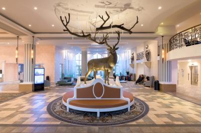 Chambre d'hôtel lumineuse avec lit double, coin salon, rideaux jaunes, mobilier en bois et fauteuils bleus.