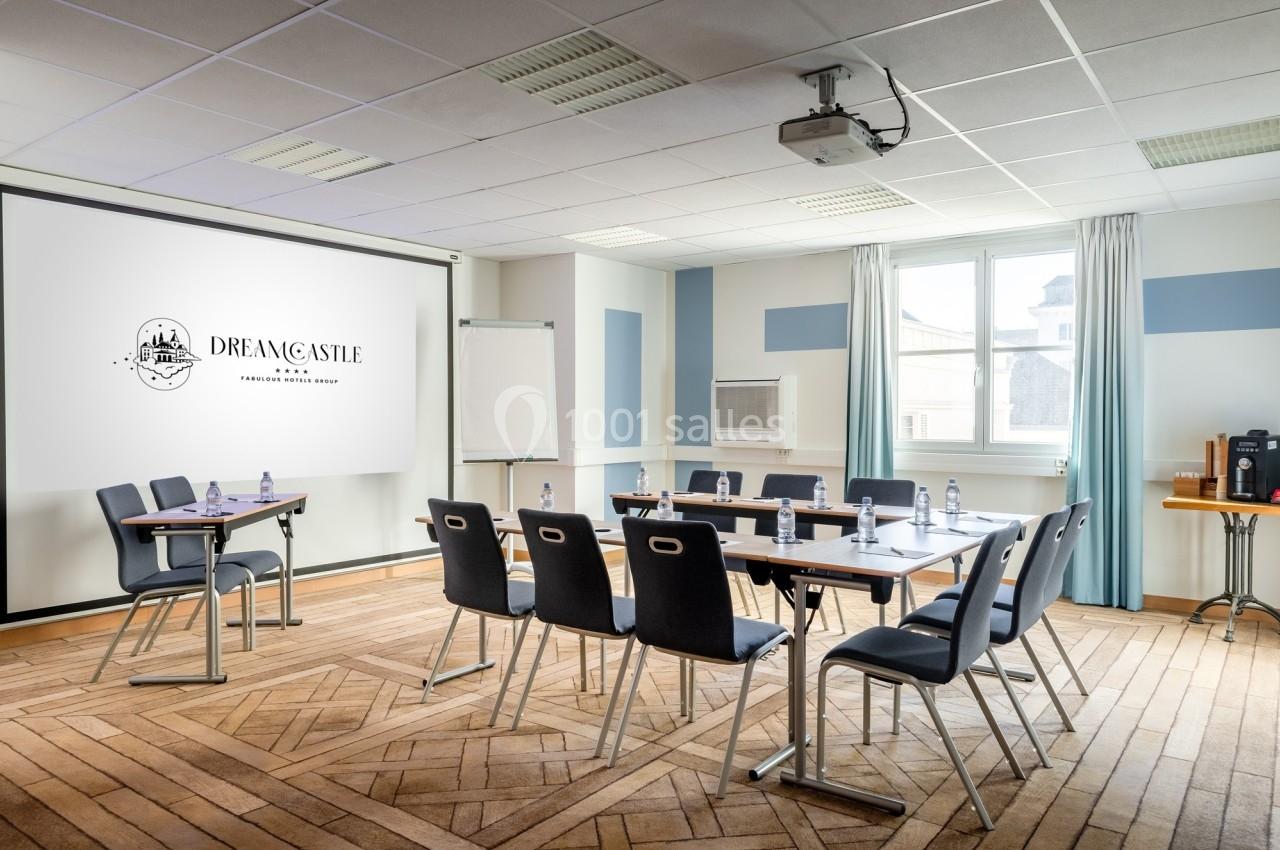 Salle de réunion lumineuse avec tables, chaises, écran de projection, paperboard et bouteilles d'eau.