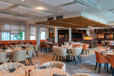 Chambre d'hôtel lumineuse avec lit double, coin salon, rideaux jaunes, mobilier en bois et fauteuils bleus.