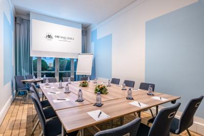 Chambre d'hôtel lumineuse avec lit double, coin salon, rideaux jaunes, mobilier en bois et fauteuils bleus.