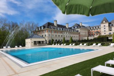 Chambre d'hôtel lumineuse avec lit double, coin salon, rideaux jaunes, mobilier en bois et fauteuils bleus.