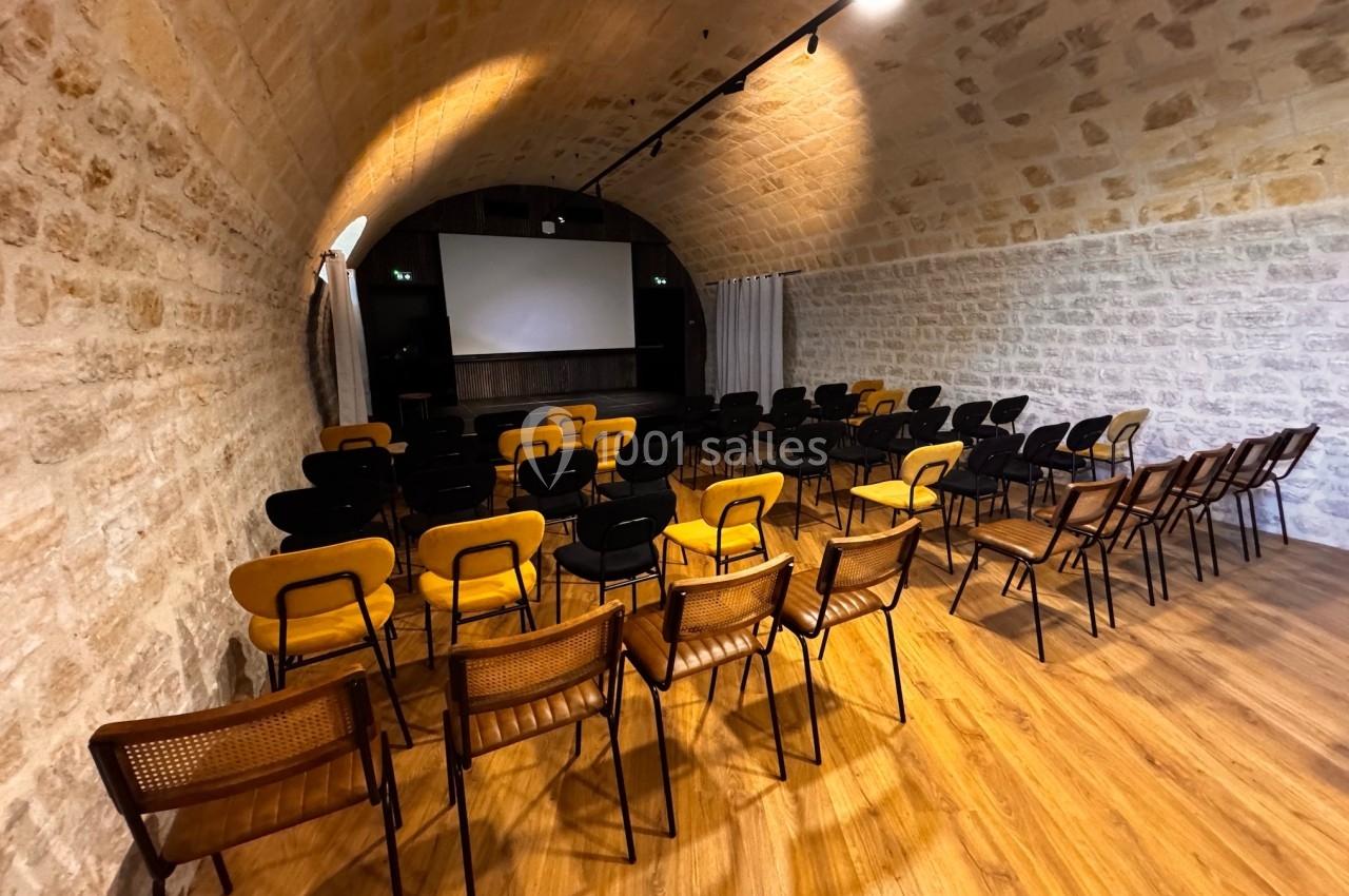 Salle voûtée en pierre avec des rangées de chaises disposées face à un écran de projection.