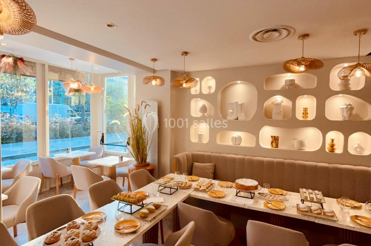 Salle de restaurant lumineuse avec tables dressées, chaises beiges et étagères décoratives éclairées au mur.