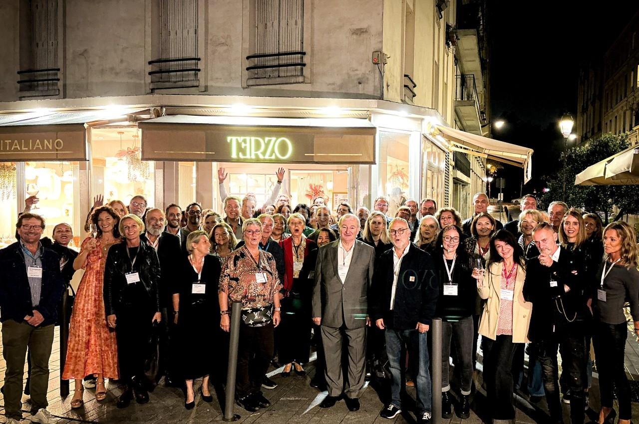 Un groupe de personnes posant devant un restaurant éclairé la nuit, dans une rue urbaine.