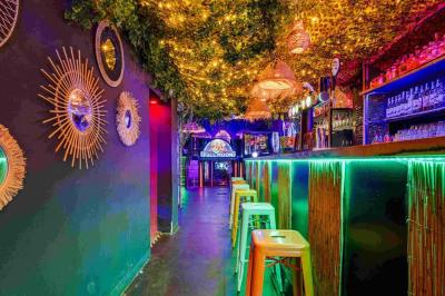 Miniature Location salle Lille (Nord) - Fullmoon #11 Façade d'un bar avec une décoration végétale, des néons roses et des tabourets noirs sur le trottoir.