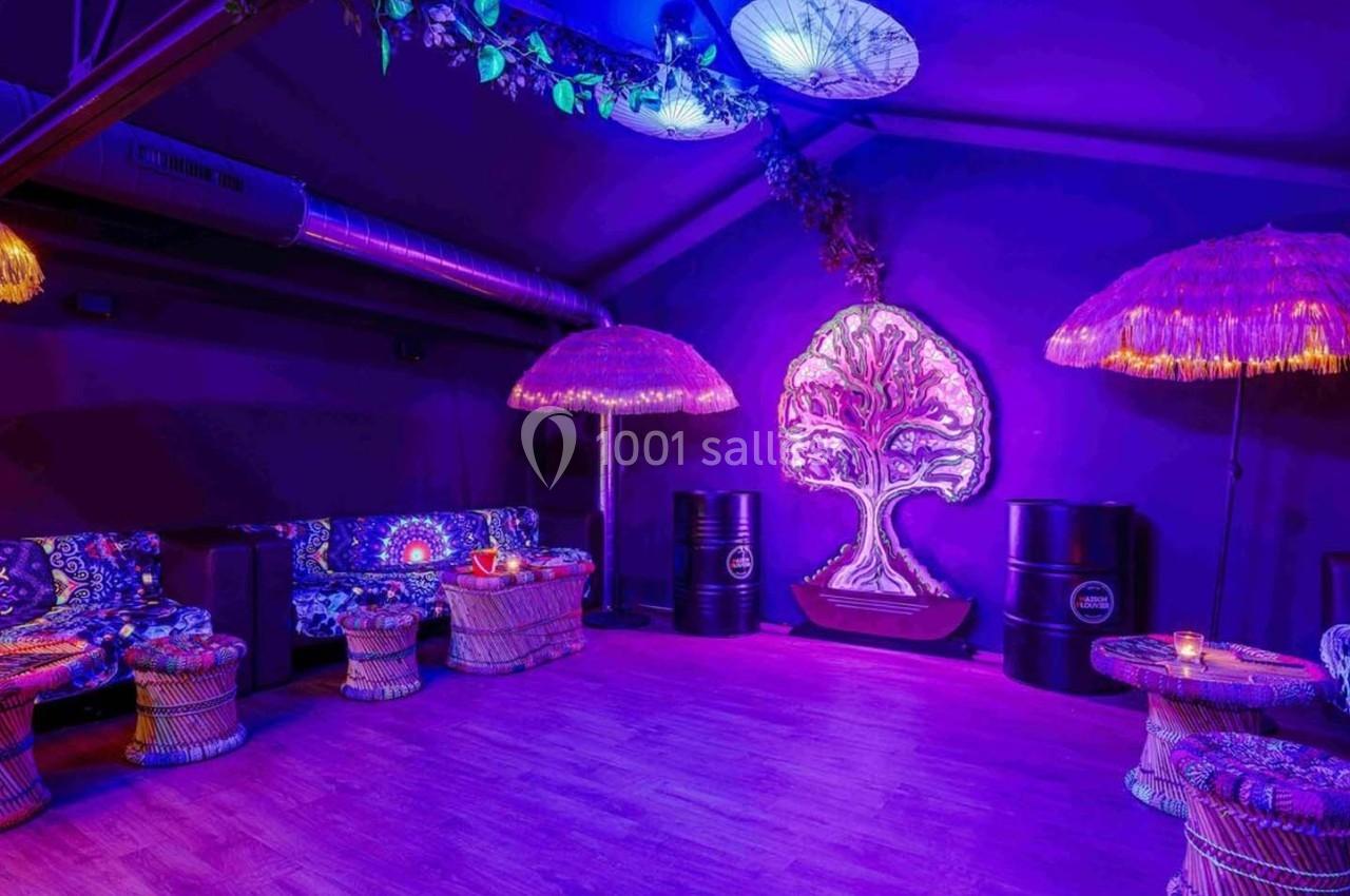Salle décorée avec des lumières violettes, des meubles en rotin, des motifs psychédéliques et un arbre lumineux au mur.