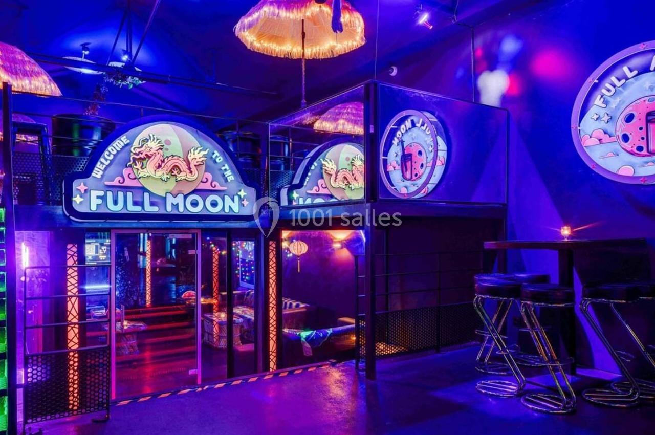 Intérieur d'un bar coloré avec éclairage néon, enseignes lumineuses ’Full Moon’ et tabourets près de tables hautes.