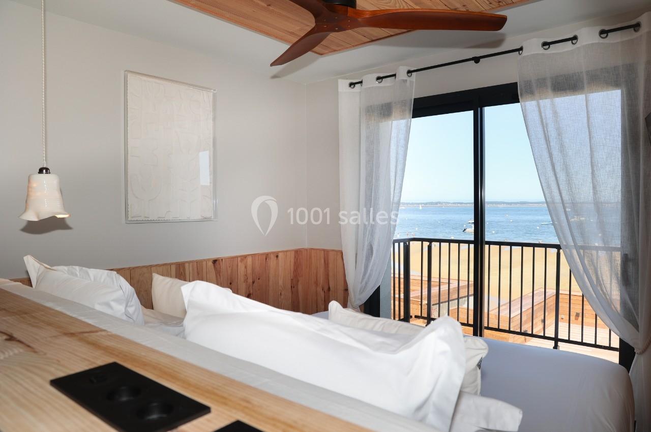 Chambre lumineuse avec lit en bois, grandes fenêtres donnant sur une terrasse et vue sur la mer.