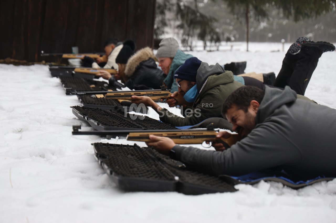 Des personnes allongées sur la neige participent à une séance de tir avec des carabines, en extérieur.
