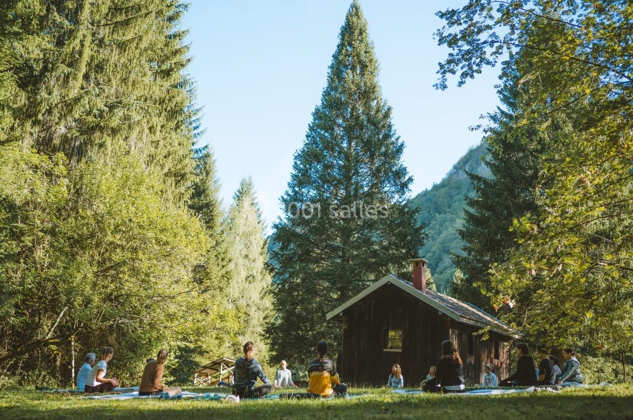 Groupe de personnes assises en cercle dans une clairière boisée près d'une petite cabane en bois.