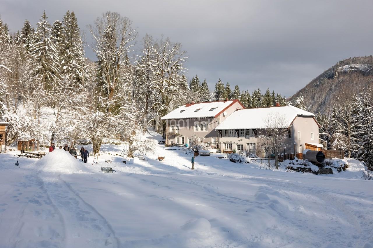 Paysage enneigé avec des bâtiments entourés d'arbres, des personnes profitant de la neige au premier plan.