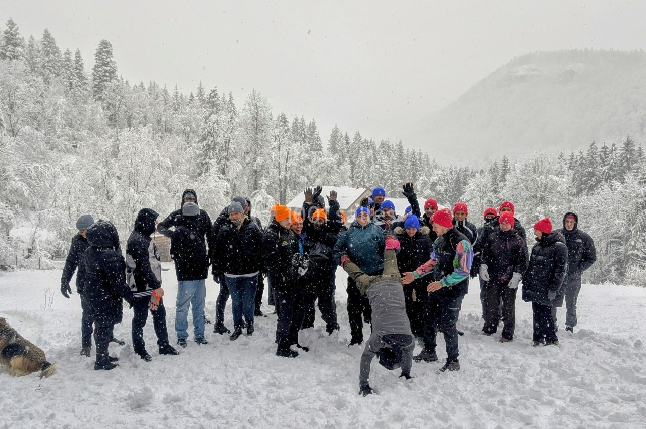 Un groupe de personnes habillées chaudement pose dans un paysage enneigé avec des arbres et des collines en arrière-plan.
