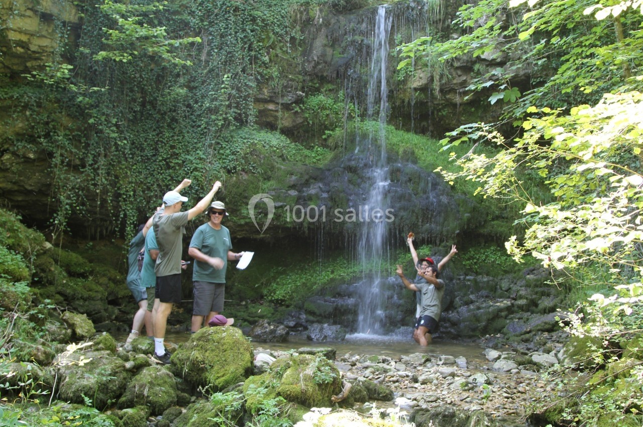 Des personnes profitent d'une cascade entourée de végétation dense, l'une d'elles se tenant dans l'eau.