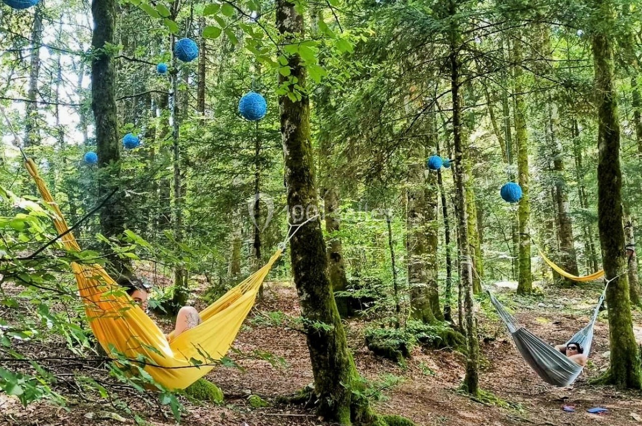 Des personnes se reposent dans des hamacs colorés suspendus entre des arbres dans une forêt décorée de lanternes bleues.