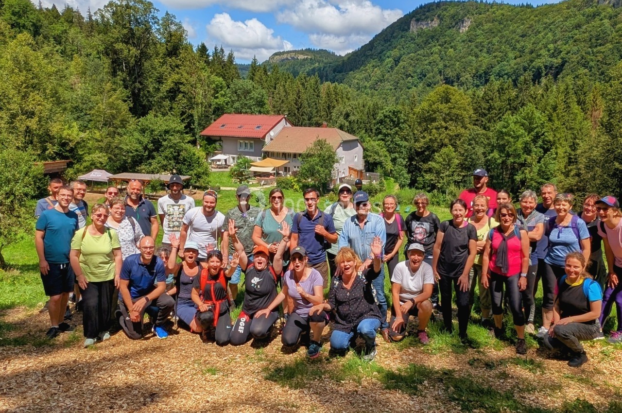 Un groupe de personnes pose en extérieur devant un paysage verdoyant avec des collines et un bâtiment en arrière-plan.