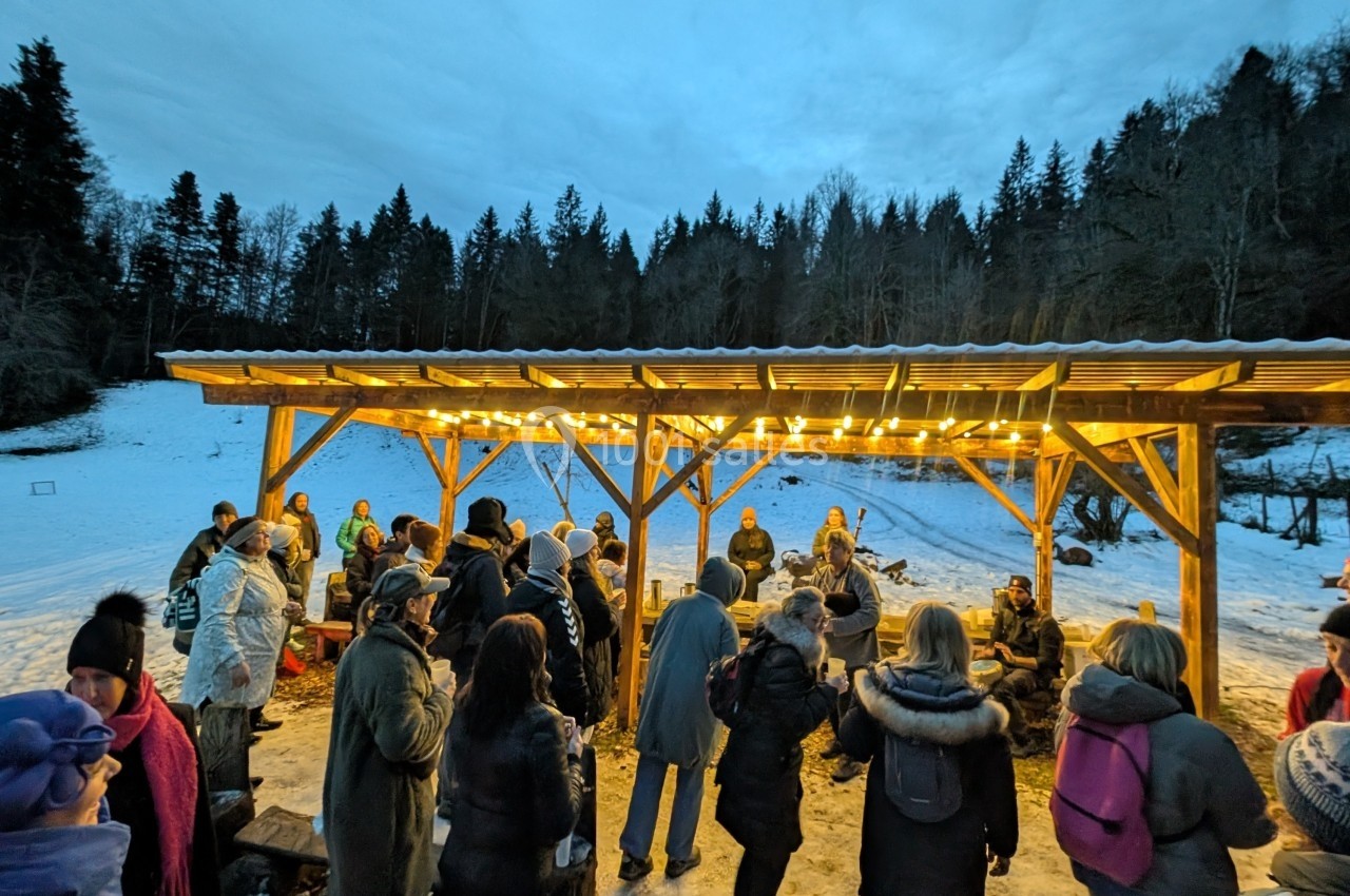 Groupe de personnes rassemblées sous un abri éclairé en bois, entouré de neige et d'arbres en arrière-plan.