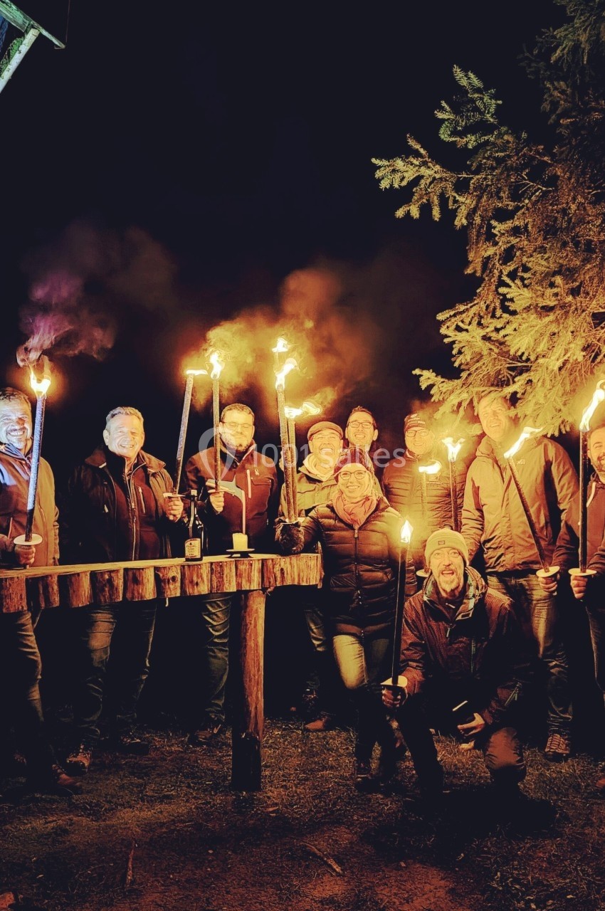 Un groupe de personnes tenant des torches allumées, rassemblées dehors la nuit près d'une cabane en bois.