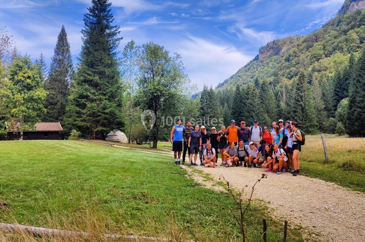 Un groupe de personnes pose sur un chemin en pleine nature, entouré de montagnes, arbres et prairies.