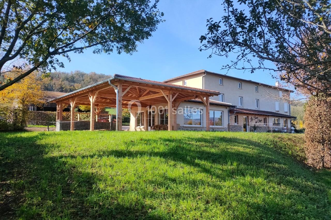 Bâtiment avec terrasse couverte en bois, entouré de verdure et d'arbres, sous un ciel dégagé.