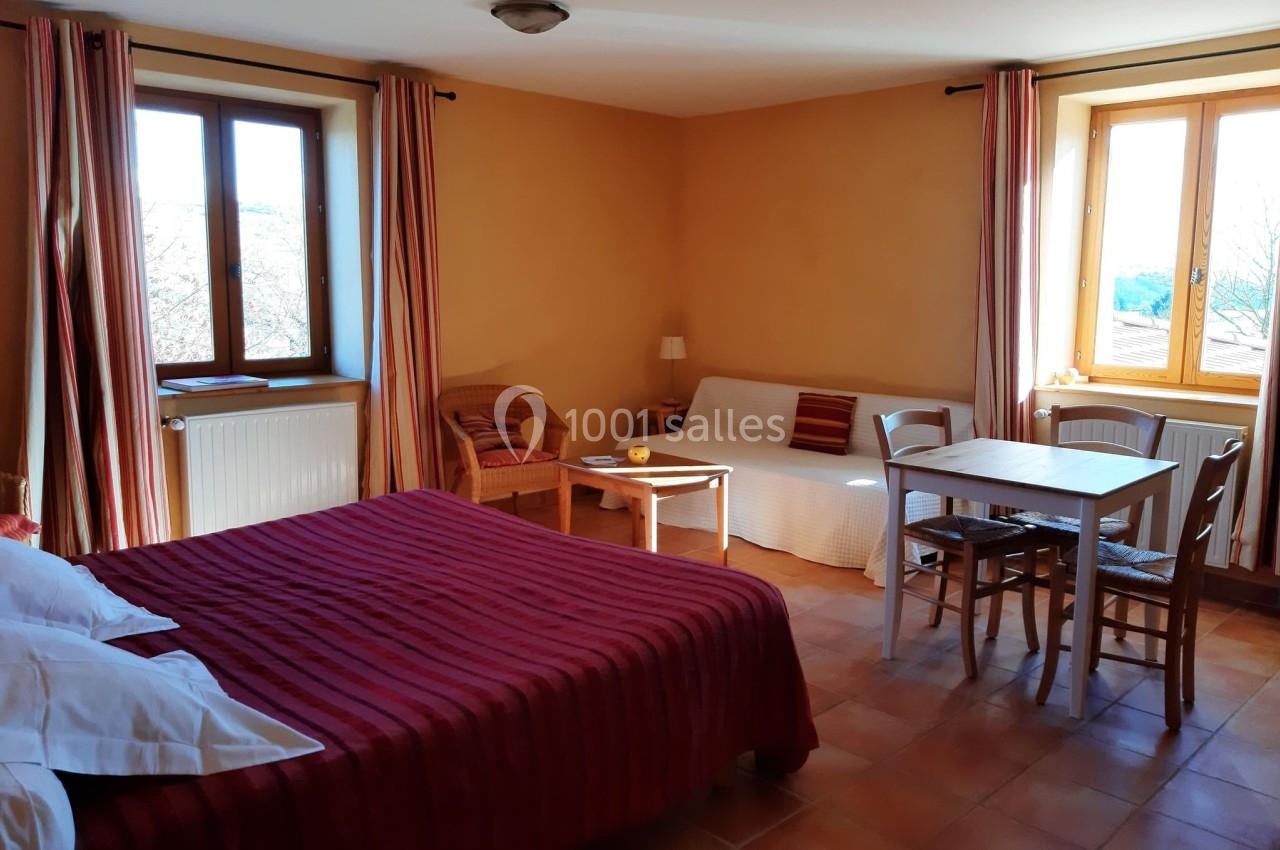 Chambre lumineuse avec lit double, canapé, table, chaises et fenêtres donnant sur un paysage extérieur.