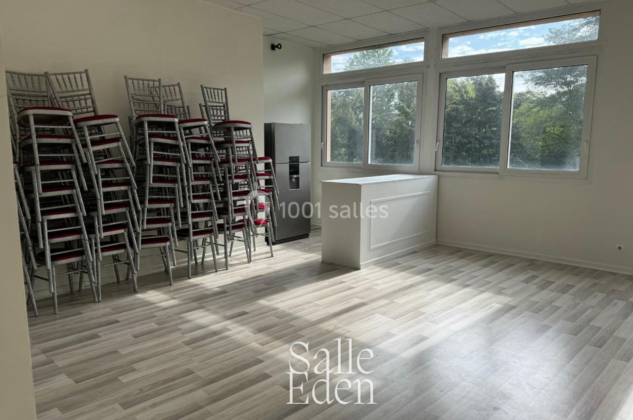 Salle lumineuse avec parquet clair, empilement de chaises à gauche, comptoir blanc et grandes fenêtres donnant sur un espace…