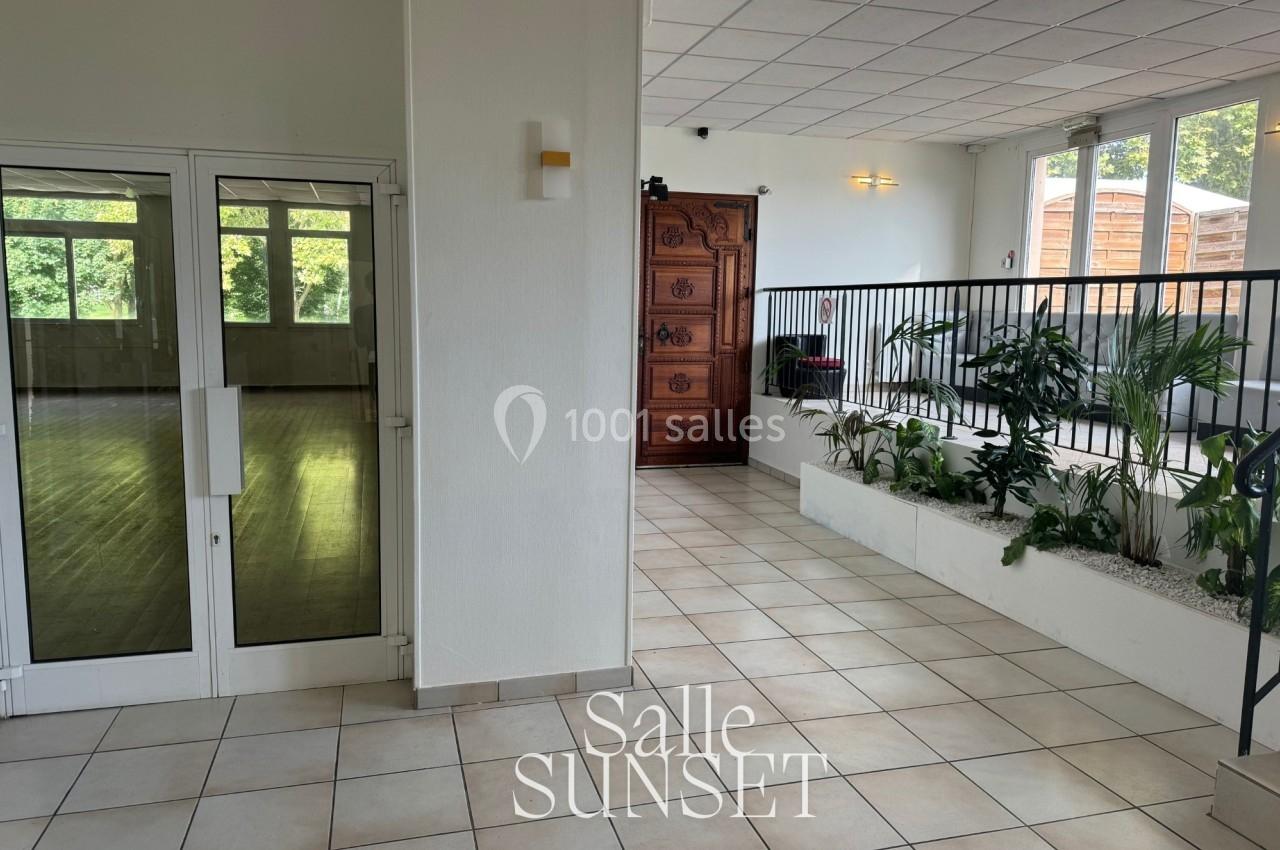 Entrée d'une salle avec portes vitrées, plantes en pot et lumière naturelle provenant de grandes fenêtres.