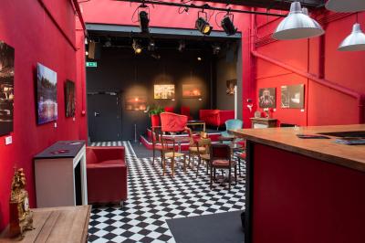 Espace salon avec canapés et fauteuils rouges, table basse en bois, plantes et photos encadrées sur un mur sombre.