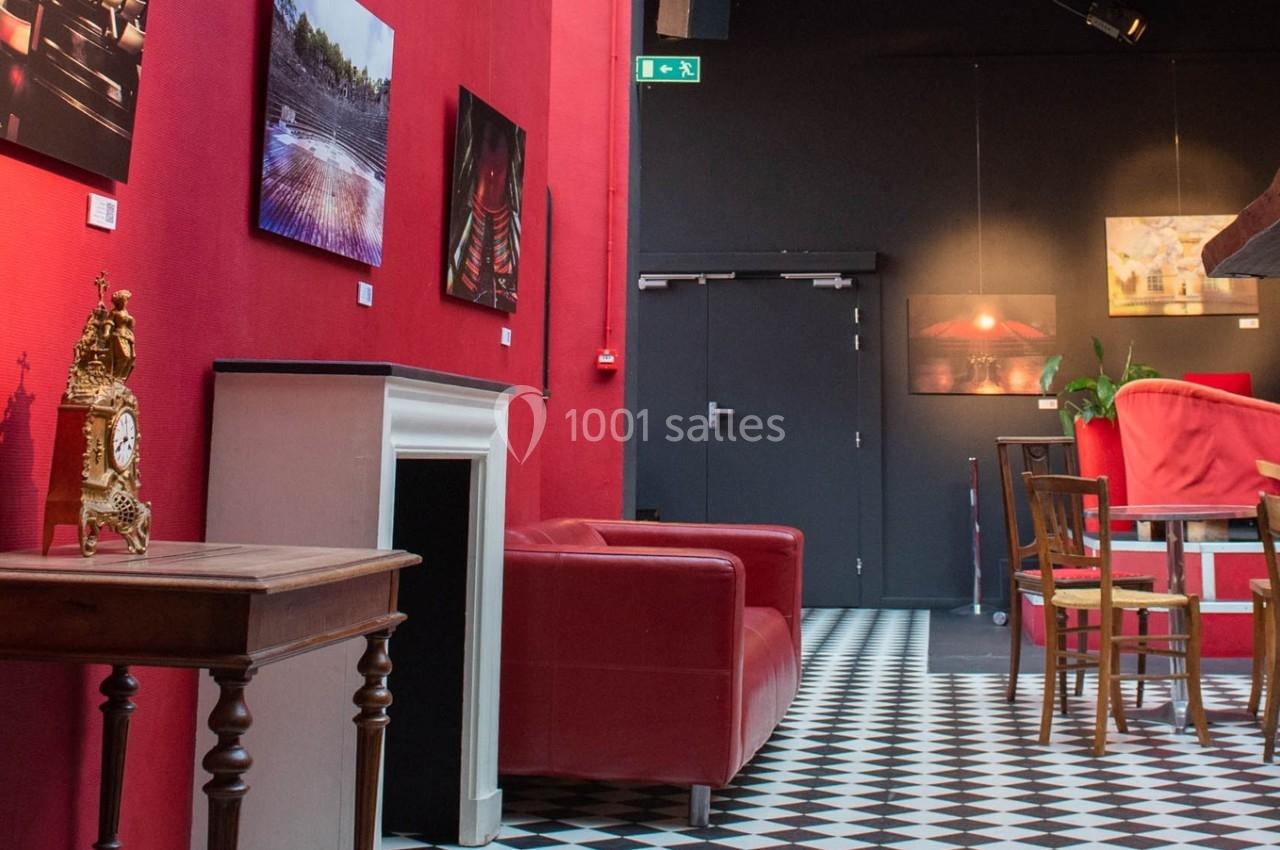 Salon avec murs rouges, sol à carreaux noirs et blancs, mobilier en bois, fauteuils rouges et décorations murales.