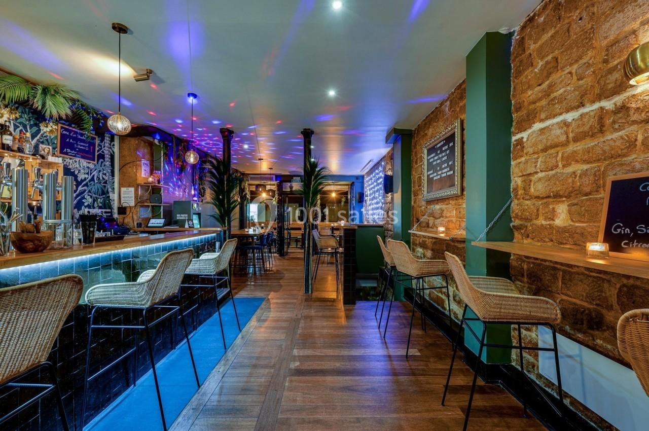 Intérieur d'un bar avec comptoir en bois, tabourets en rotin, éclairage tamisé et décorations murales colorées.