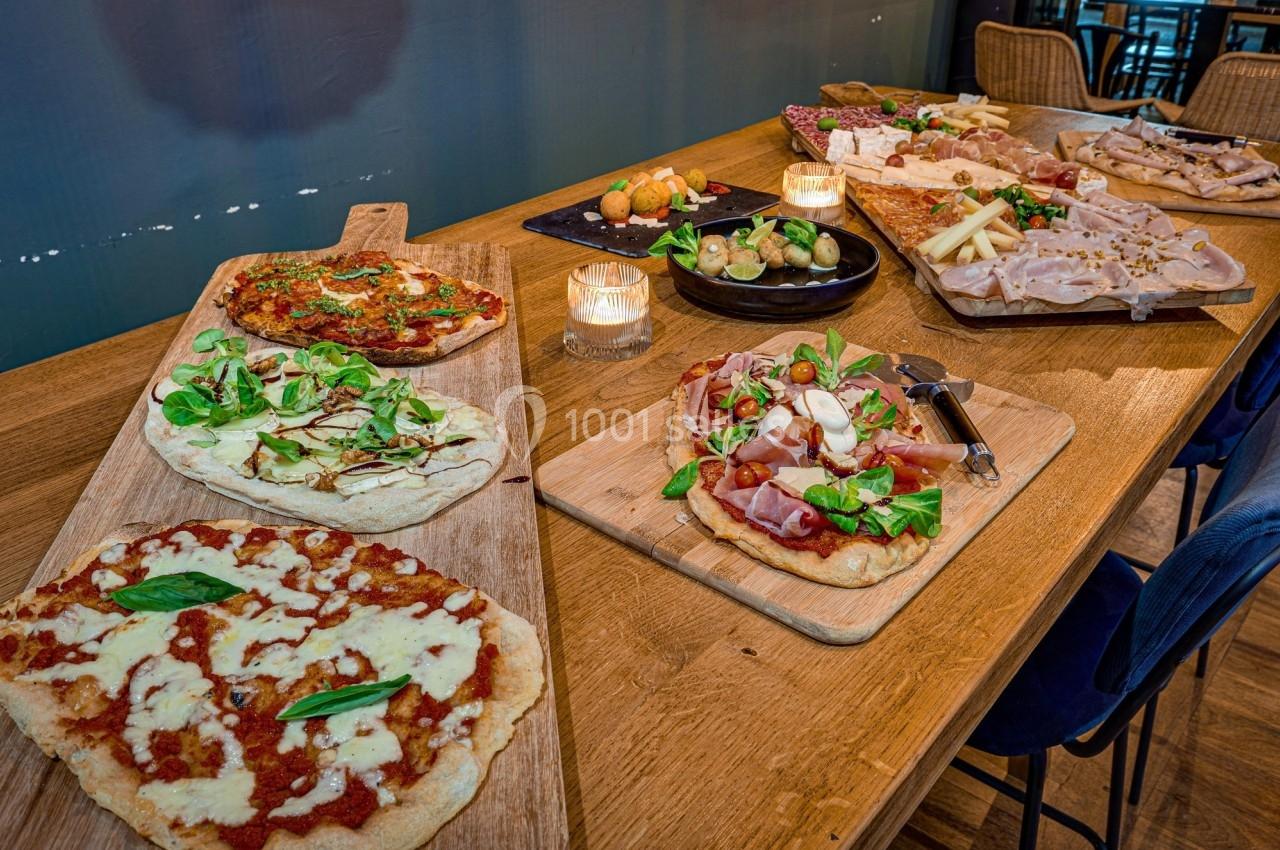 Plateau de pizzas variées garnies de légumes, charcuteries et fromages, disposé sur une table en bois avec des bougies.
