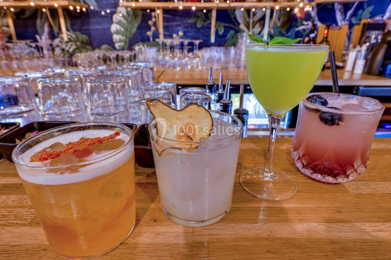 Quatre cocktails variés disposés sur un comptoir en bois, avec des décorations et des verres en arrière-plan.