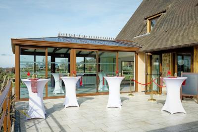 Aire de jeux en bois sur sol sablonneux, entourée de verdure et située près de bâtiments ruraux sous un ciel bleu.