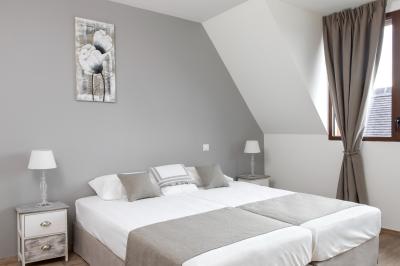 Aire de jeux en bois sur sol sablonneux, entourée de verdure et située près de bâtiments ruraux sous un ciel bleu.