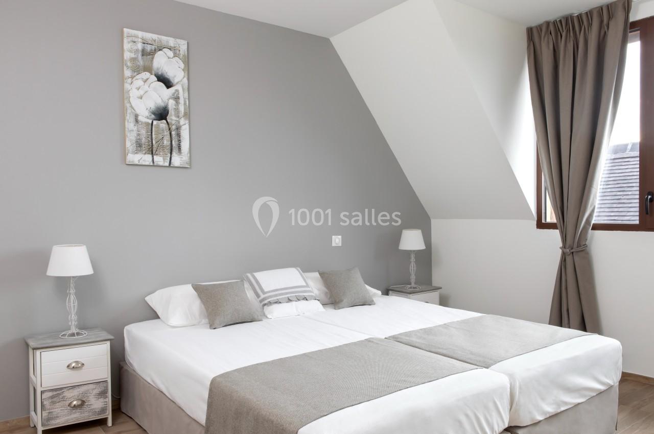 Chambre lumineuse avec un lit double, des murs gris, des rideaux assortis et deux tables de chevet avec lampes.