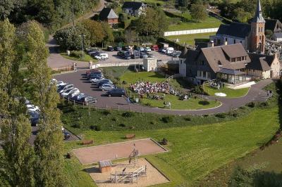 Aire de jeux en bois sur sol sablonneux, entourée de verdure et située près de bâtiments ruraux sous un ciel bleu.