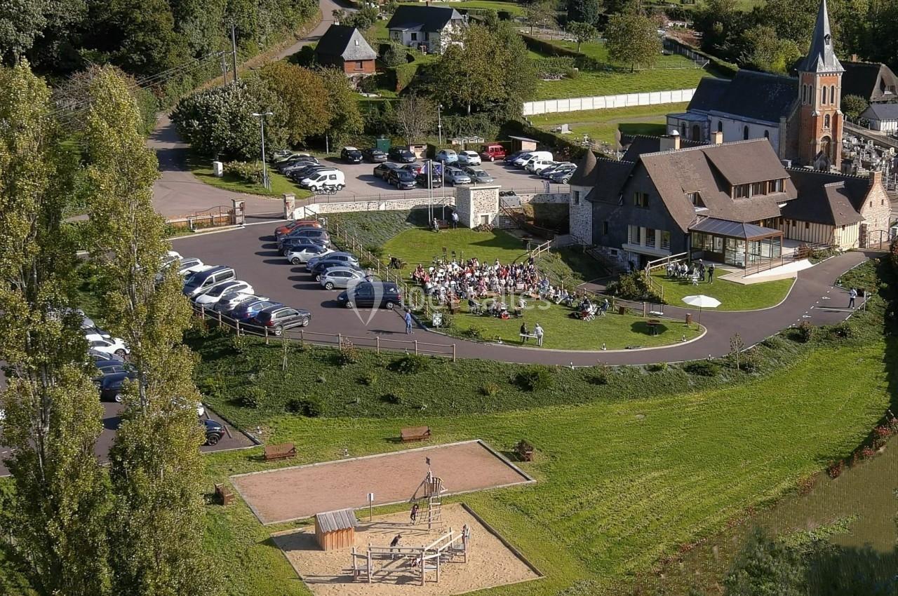 Vue aérienne d'un village avec une église, un parking, une aire de jeux et un rassemblement de personnes en extérieur.