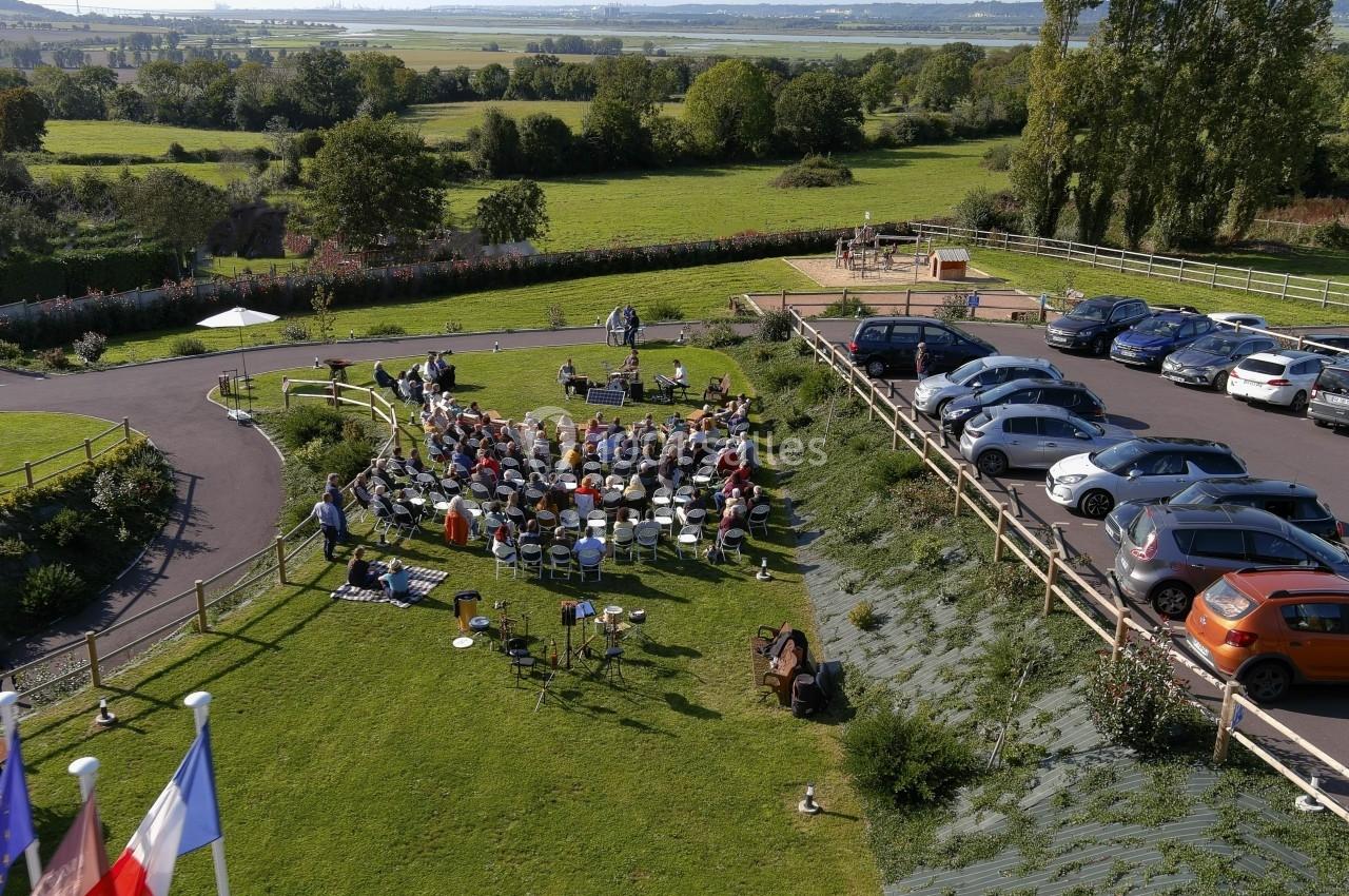 Vue aérienne d'un rassemblement en plein air avec des chaises disposées sur une pelouse, entouré de voitures et de paysages…