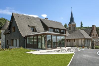 Aire de jeux en bois sur sol sablonneux, entourée de verdure et située près de bâtiments ruraux sous un ciel bleu.