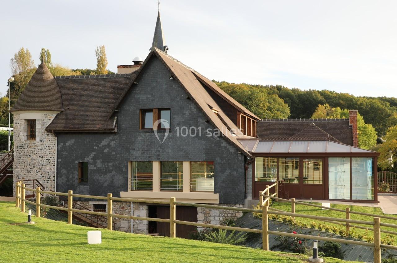 Bâtiment en pierre et ardoise avec une tour, entouré de verdure et clôturé par une barrière en bois.