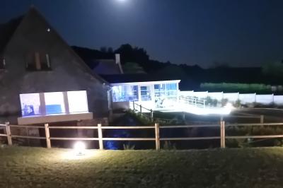 Aire de jeux en bois sur sol sablonneux, entourée de verdure et située près de bâtiments ruraux sous un ciel bleu.