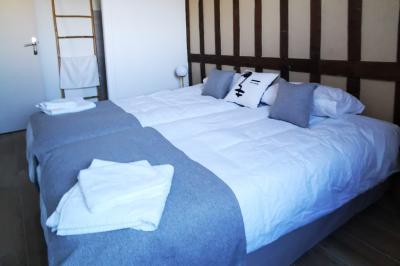 Aire de jeux en bois sur sol sablonneux, entourée de verdure et située près de bâtiments ruraux sous un ciel bleu.